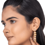 The girl is wearing a long earrings in her ear and is showing it with her hand